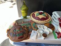 Photo showing all items in lot including yellow lidded glass jar, ceramic wall art, lidded pie dish, wooden bowl, and miniature ceramic bathroom set.