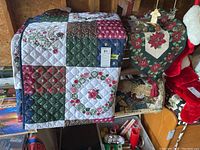 Photo showing the Christmas-themed quilted bedspread folded over a surface, displaying patchwork squares in green, red, white, and blue with holiday motifs.