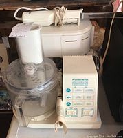 Proctor Silex 2-speed food processor in front, Black & Decker meat slicer behind it on a shelf, with several cords and a coffee maker partially visible.