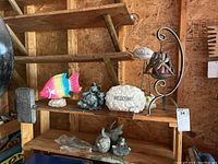 Shelf with colorful painted metal fish, cast stone 'Welcome' plaque, two stoneware frog figurines, and other netural-colored stoneware or composite garden ornaments.
