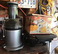 Photo of the juicer, electric grill and boxed manual pasta maker together on wooden surface in garage