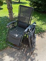 Two folding zero gravity lawn chairs showing metal frames, mesh seats with holes, and rusted joints, one chair folded and one unfolded
