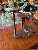 Wooden plant stand shown from an angle with a view of the three different height round platforms, wood finish showing wear.