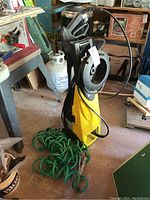 Yellow Craftsman CPW 1650 pressure washer with attached hose and green garden hose on floor.