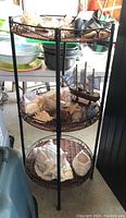 Top to bottom view of three-tier metal and wicker shelf holding ceramic shells, real shells, glass elephant figurines, and a ship model.