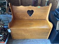 Front view of the wooden storage bench showing the heart-shaped cutout and hinged seat.