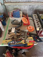 Photo showing various hand tools including clamps, saws, a propane torch, rolls of tape, and the Wagner Power Painter manual on a table.
