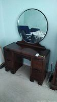 Vintage solid wood vanity table with round mirror shown assembled. The mirror is round, wooden framed and visible wear on edges of the table is present. The mirror is in place but detached for transport.