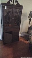Full view of vintage solid wood cabinet showing upper glass doors with wood trim, lower solid doors and drawer, standing on hardwood floor.
