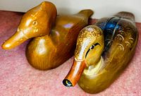 Close-up of two carved wood duck decoys, showing painted details and signing on the underside.