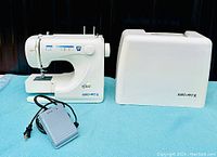 Euro-Pro white serger sewing machine on blue surface with attached foot pedal and power cord alongside matching hard plastic carrying case.