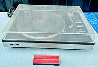 Turntable closed with dust cover on, showing JVC branding and red velvet-lined cartridge case in front.