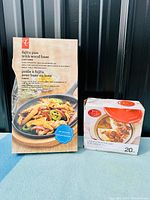 Photo showing boxed cast iron fajita pan with wooden base and boxed cast iron brie baker kit with orange lid