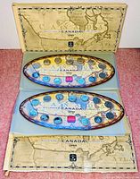Two open display cases showing 1999 Canada quarters with various proof-like designs arranged on map-themed inserts inside a box.