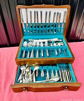 Full view of the wooden chest containing the three compartments filled with flatware items, showing the quantity and various types of utensils.