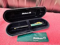 Pelikan rollerball pen inside black presentation box with guarantee card on red surface.