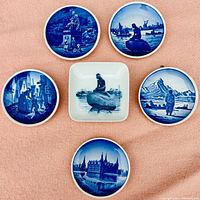 Six Royal Copenhagen miniature plates arranged on fabric background showing their blue and white scenic designs.