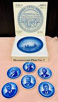 Image of boxed set showing six smaller presidential plates and one large bicentennial plate, deep blue tones, clear and legible details.