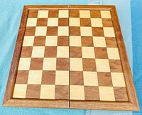 Top-down view of the closed wooden folding chessboard showing the classic alternating light and dark wood squares and polished edges.