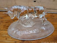 Front angle view of a clear glass bull figurine on an oval glass base, showing the bull in a charging pose with detailed horns and musculature.