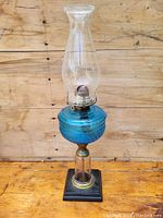 Full view of antique blue glass coal oil lamp with clear chimney on black base.