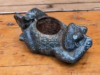 Top angled view of dark cast iron frog figurine lying on back with hollow cavity in center.