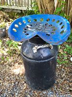 Antique milk can topped with blue cast iron tractor seat chair outdoors on gravel and leaves