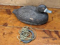 Photo showing the full duck decoy with visible paint wear, tack eyes, and attached rope on wooden surface.