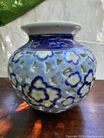 Front angle view of the pottery vase showing blue floral painted decorations with pierced lattice style cut-outs on the body.