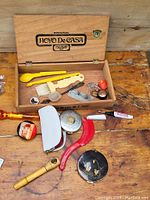 Wooden box labeled 'Hoyo De Casa' with assorted vintage advertising kitchen items and tools spread on wooden surface