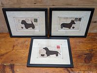 Three framed dog-themed prints on a wooden surface showing different dog silhouettes.