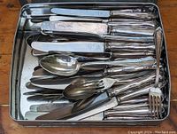 Top view showing a large assortment of mixed silver cutlery including knives, forks, and spoons inside a metal tray.