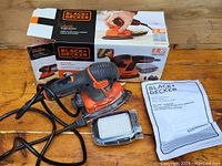 Overview of Black & Decker The Mouse detail sander with box, manual, and sanding pad attachment on a wooden surface.