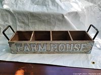 Front and side view of wooden organizer with the word FARMHOUSE on the front in raised letters, showing four separate compartments and metal handles on each side.