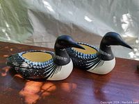 Pair of ceramic loon planters shown from side angles on a wooden surface with a fabric background under natural light, highlighting the paint details and planter openings.