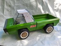Side view of vintage green metal tin toy truck with large rubber tires and clear windshield, branded Buddy L.