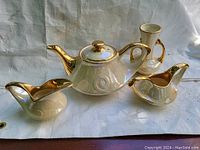 Full view of tea set including teapot, creamer, sugar bowl, and vase, showing pearl finish and gold trim.