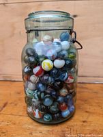 Clear vintage glass jar filled with colorful glass marbles. The jar is vintage style with a metal clasp.