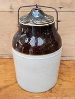 Full front view of vintage ceramic cheese crock, showing two-tone brown and cream ceramic body and metal handle with round lid on top.