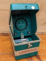 Front view of the vintage Lowrance fishfinder with case lid open, showing circular dial and control knobs.