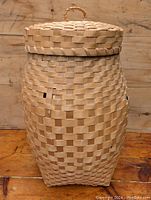 Front view of the handmade woven split ash lidded basket showing the tapered shape, woven checkerboard pattern, and lid with loop handle.