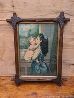 Full view of vintage Victorian framed colored print showing two children, titled "The Sisters", in wooden frame with leaf decorations at corners.