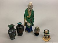 Photo showing the full lot including the Mudman figure, cloisonné egg on a black base, and three cloisonné bud vases, arranged on a white surface.