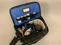 Open black padded carrying case with blue interior holding several film canisters and lens accessories.