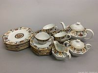 Full set including plates, teacups, teapot, creamer, and sugar bowl laid out together on grey background.