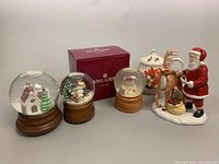 Photo showing (2) crystal ball musical snowglobes, Lenox Santa and reindeer figurine, Sadler poinsettia teapot, Royal Albert box, and candy dish.