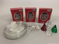 Photo showing three boxed Waterford 2011 Train Engine Crystal Ornaments, eight stacked transparent MCM Arcoroc plates, three mini Christmas trees in red, green and clear glass, and a clear shining star paperweight.