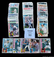 Photo showing multiple stacks of 1984 O.P.C. baseball cards with team names visible such as Tigers, Angels, Mets, Orioles, Brewers, Astros, Cubs, and Expos.