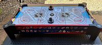 Full front view showing NHL ice rink graphic and NHL team logos on sides of tabletop air hockey game.