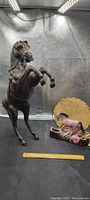 Photo showing a 24-inch leather rearing horse statue with bridle and a vintage ceramic horse lamp featuring a pink horse figure and yellow cracked lampshade, placed side by side on a black surface with ruler for scale.